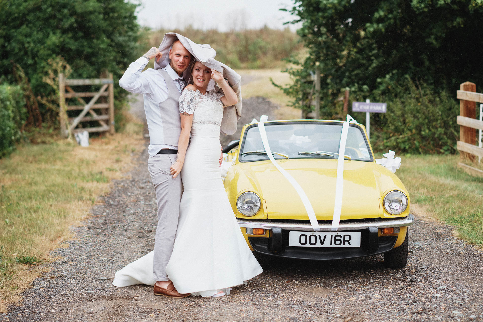 Wedding couple sheltering under a coat from a rain shower, yellow vintage car, All Manor of Events, Henley, Heffs Photography, Suffolk Weddings,